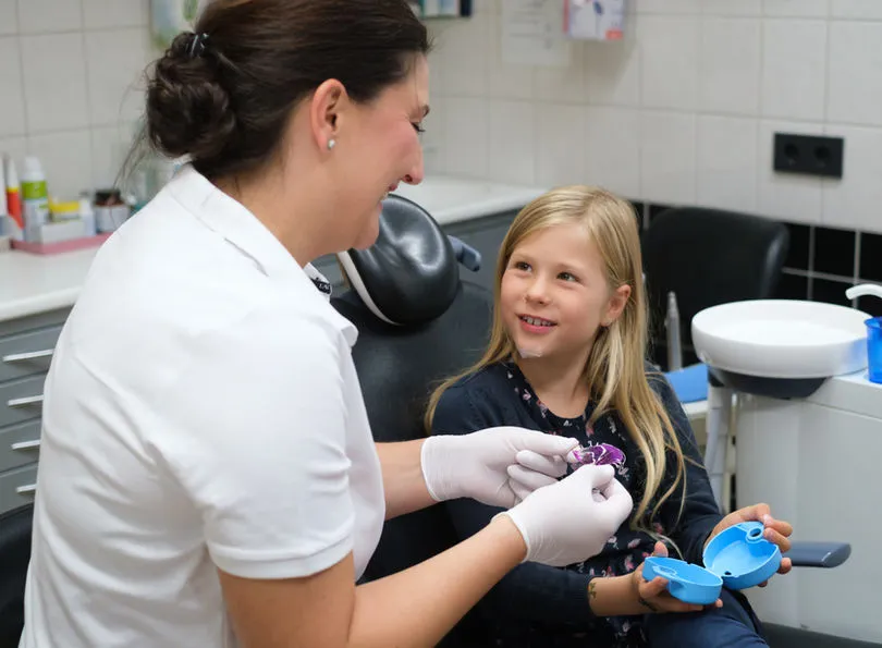 Zahnärztin zeigt einem Mädchen eine herausnehmbare Zahnspange